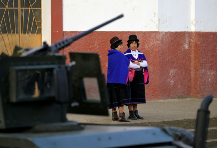 Un blindé de l'armée colombienne passe devant deux femmes de l'éthnie Misak à Silvia, dans le département du Cauca, le 22 mai 2026 ( AFP / Joaquin SARMIENTO )