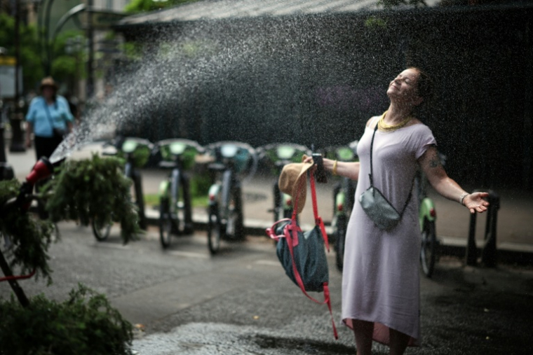 Une femme se rafraîchit devant un tuyau d'arrosage à Paris, le 18 juin 2026 ( AFP / Simon WOHLFAHRT )