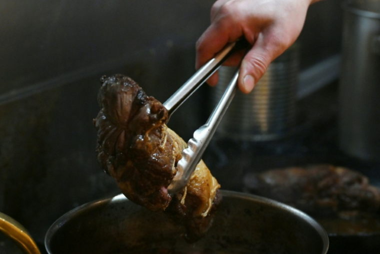 Le chef Kiyoshi Fujimoto met un morceau de viande d'ours dans une marmite pour les clients de son restaurant à Sapporo, dans la préfecture d'Hokkaido, le 9 décembre 2025 au nord du Japon ( AFP / GREG BAKER )
