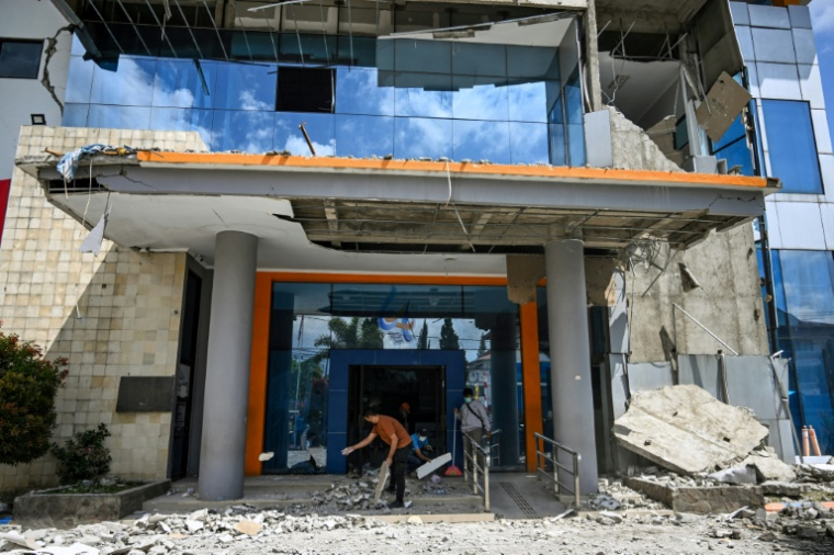 Des employés ramassent des gravats devant une banque après le puissant séisme qui a secoué l'île indonésienne de Florès, dans l'est de l'archipel, le 16 août 2026 à Ruteng, à quelque 158 kilomètres à l'ouest de l'épicentre  ( AFP / JUNI KRISWANTO )