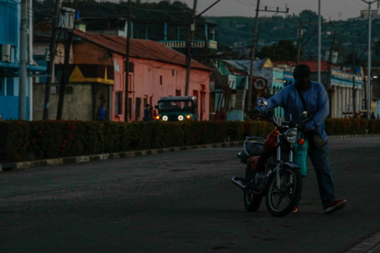 Un homme déplace une moto lors d'une panne de courant, le 14 mai 2026 à Santiago de Cuba ( AFP / STRINGER )