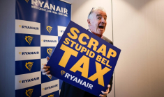 Michael O'Leary, PDG de la compagnie aérienne Ryanair pose avec une pancarte reprochant à la Belgique une série de taxes "stupides", lors d'une conférence de presse à Bruxelles le 14 janvier 2026 ( AFP / Simon Wohlfahrt )