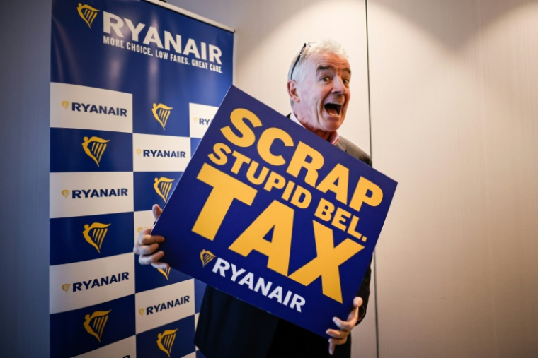 Michael O'Leary, PDG de la compagnie aérienne Ryanair pose avec une pancarte reprochant à la Belgique une série de taxes "stupides", lors d'une conférence de presse à Bruxelles le 14 janvier 2026 ( AFP / Simon Wohlfahrt )