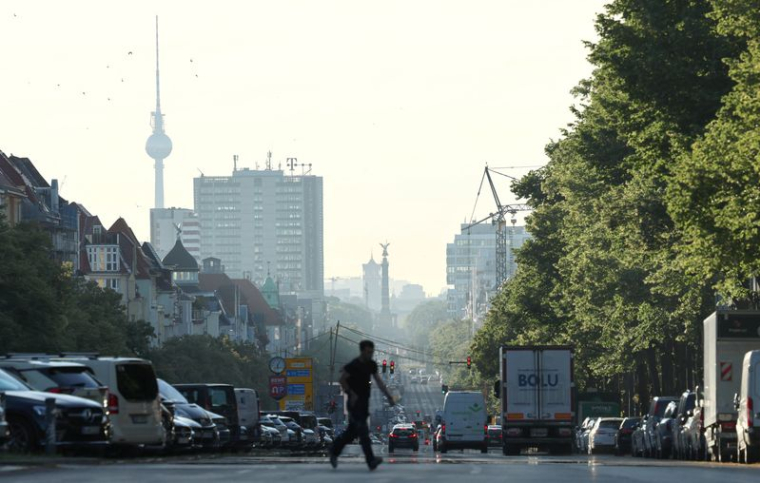 Les véhicules circulent en cette heure de pointe matinale, tandis que la brume du lever du soleil illumine l'horizon de Berlin