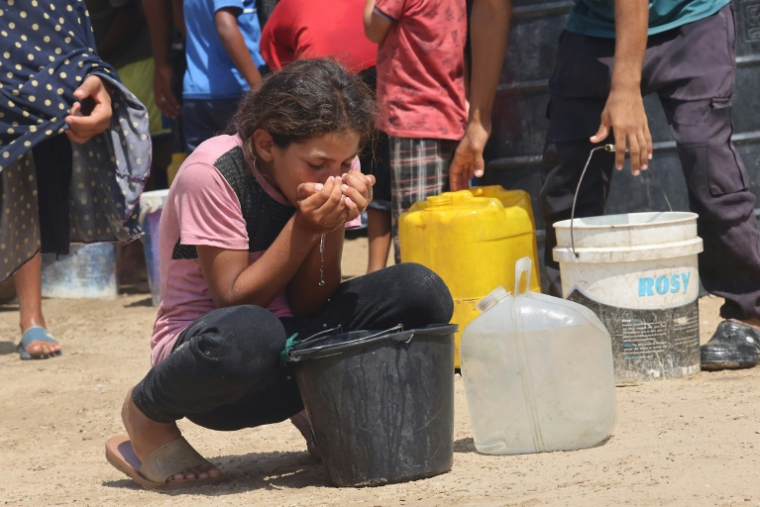 Une fillette boit de l'eau dans un seau en plastique pendant que des Palestiniens déplacés font la queue pour remplir de l'eau dans la région d'al-Mawassi dans le sud de la bande de Gaza, le 14 août 2025 ( AFP / - )