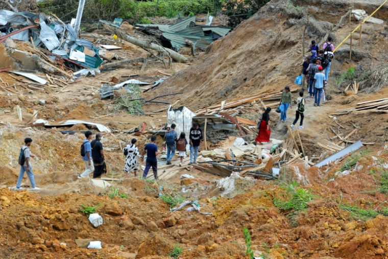Des habitants au milieu d'arbres déracinés et de maisons endommagées après des glissements de terrain provoqués par le cyclone Ditwah dans le village d'Ulapane, près de la ville de Nawalapitiya, dans le district de Kandy, le 7 décembre 2025 au Sri Lanka ( AFP / - )