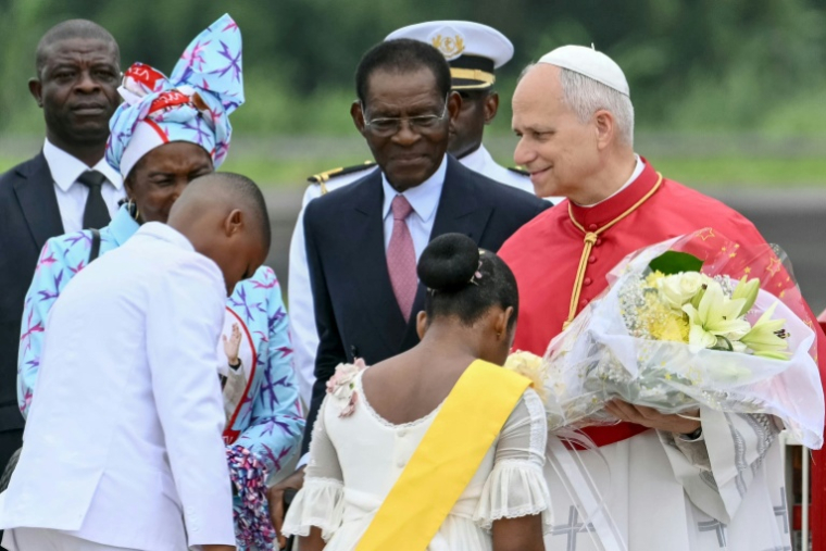 Le pape Léon XIV (à droite) reçoit des fleurs d'enfants alors qu'il est accueilli par le président de Guinée équatoriale Teodoro Obiang Nguema Mbasogo (au centre) à son arrivée à l'aéroport international de Malabo à Malabo le neuvième jour d'un voyage apostolique de 11 jours en Afrique, le 21 avril 2026. ( AFP / Alberto PIZZOLI )