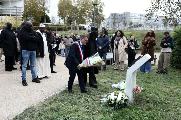 Le frère de Bouna, Siyakha (g), et son père Seydou (2e g) debout près du maire de Clichy-sous-Bois, Olivier Klein (c), qui dépose des fleurs devant une plaque à l'extérieur du lycée Robert Doisneau lors d'une cérémonie  marquant le 20e anniversaire de la mort des adolescents Zyed Benna et Bouna Traoré, le 27 octobre 2025 en Seine-Saint-Denis ( AFP / Thibaud MORITZ )