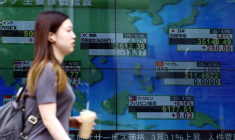 Une femme passe devant un écran électronique affichant les indices boursiers des pays asiatiques à l'extérieur d'une maison de courtage à Tokyo