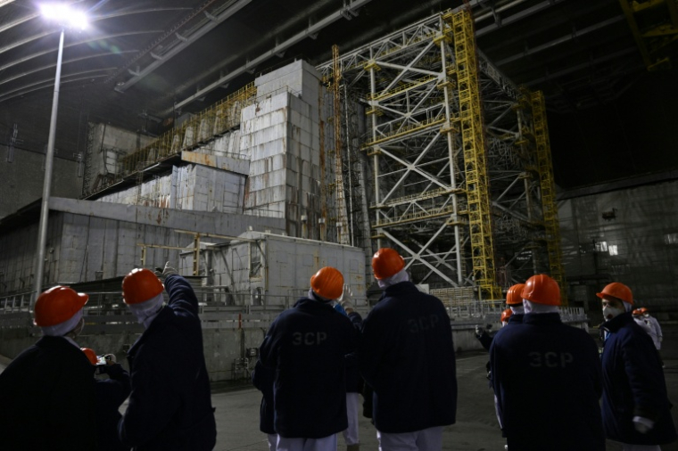Des représentants de Greenpeace et des médias devant le sarcophage recouvrant le quatrième réacteur détruit sous l'enceinte de confinement, à la centrale nucléaire de Tchernobyl, le 9 avril 2026 en Ukraine ( AFP / Genya SAVILOV )