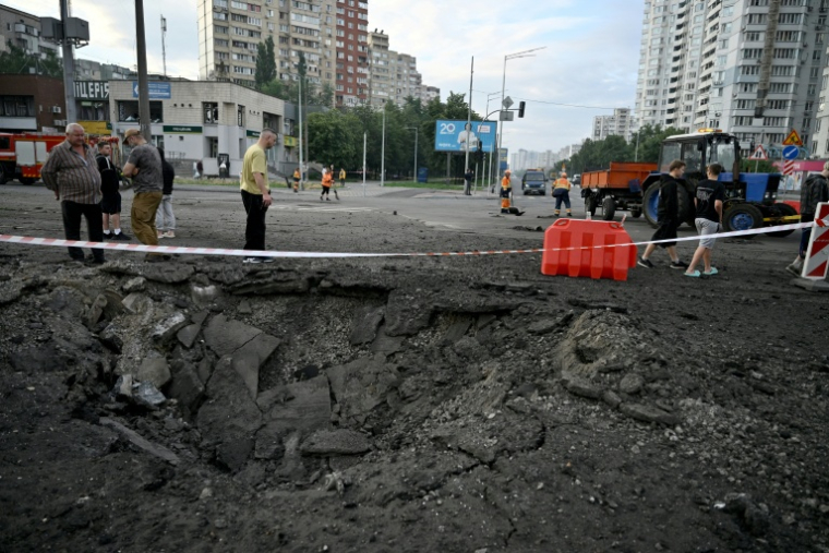 Des habitants de Kiev passent près d'un cratère causé par une frappe de missile russe sur la capitale de l'Ukraine, le 11 juillet 2026 ( AFP / Genya Savilov )