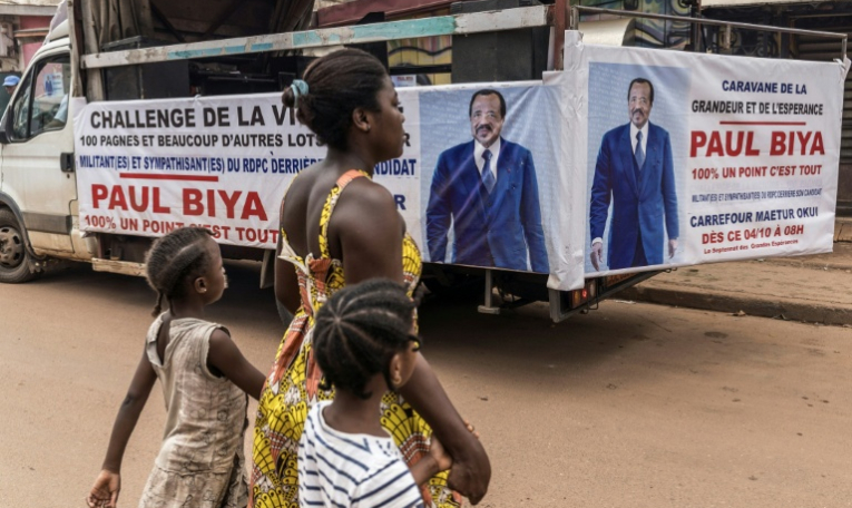 Une femme et ses enfants traversent la rue près d'un camion de campagne du président sortant du Cameroun, Paul Biya, à Yaoundé le 11 octobre 2025 ( AFP / MARCO LONGARI )
