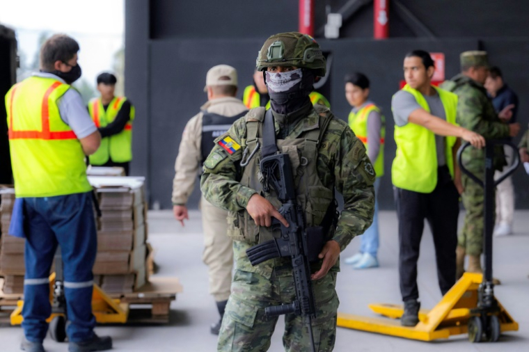 Un soldat masqué monte la garde devant des membres de la Commission électorale qui préparent le matériel de vote à la veille de l'élection présidentielle en Equateur, le 12 avril 2025 à Quito ( AFP / Luis ACOSTA )