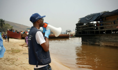 Mégaphone à la main, Yves Matwa, agent de la riposte à Ebola, passe les consignes aux passagers d’une baleinière, au port de Bende-Bende, commune de Maluku, à 70 km au nord-est de Kinshasa, le 20 août 2026 ( AFP / Sophie Douce )