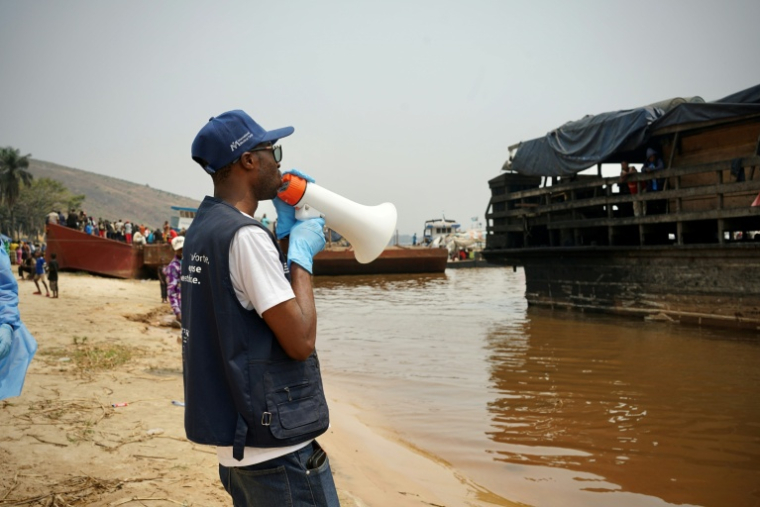 Mégaphone à la main, Yves Matwa, agent de la riposte à Ebola, passe les consignes aux passagers d’une baleinière, au port de Bende-Bende, commune de Maluku, à 70 km au nord-est de Kinshasa, le 20 août 2026 ( AFP / Sophie Douce )