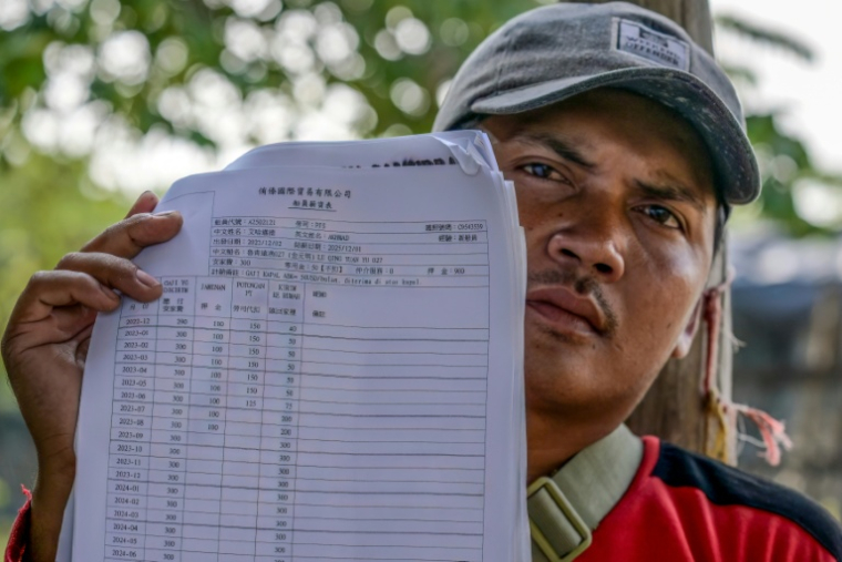 Akhmad, ancien membre d'équipage d'un navire de pêche chinois, montre son contrat et son salaire mensuel lors d'un entretien avec l'AFP au port du hameau de Bungko Lor, à Cirebon, le 10 juin 2026 en Indonésie ( AFP / BAY ISMOYO )
