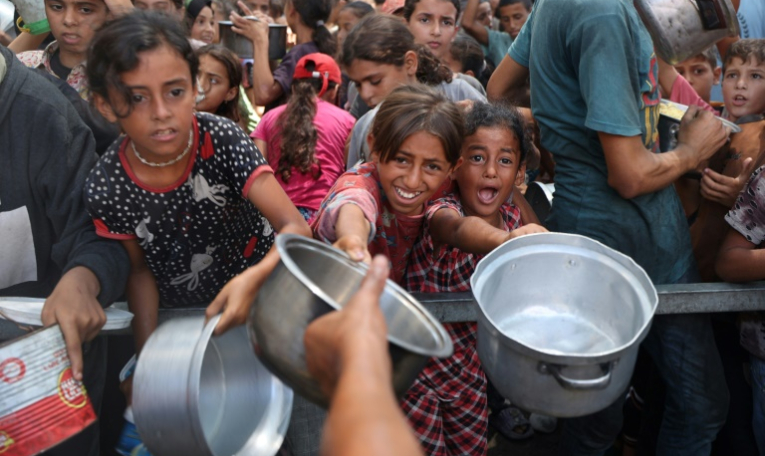 De jeunes palestiniens attendent de recevoir des repas cuisinés dans le camp de réfugiés de Nousseirat, dans le centre de la bande de Gaza, le 18 août 2025 ( AFP / Eyad BABA )