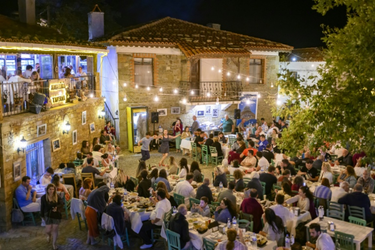 Des Grecs rassemblés dans un restaurant et assistant à des danses traditionnelles pour la fête de la Vierge, le 14 août 2026 sur l'île turque de GokceadaPeople sit at a restaurany and perform traditional Greek dance during the Feast of the Dormition of the Virgin Mary, on Gokceada (Imroz) Island, Çanakkale Province of Turkey, on August 14, 2026. Hundreds of Greeks return from Athens and around the world to Imbros each August 15 to celebrate the Virgin Mary. Like Istanbul and nearby Tenedos, the island was exempt from the 1923 population exchange between Greece and Turkey, which displaced more than 1.5 million people. ( AFP / Yasin AKGUL )