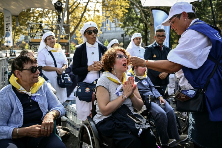 Des volontaires distribuent l'hostie aux fidèles en fauteuils roulants, lors de la messe célébrée par le pape Léon XIV sur la prairie du sanctuaire de Lourdes, le 27 septembre 2026 ( AFP / Philippe LOPEZ )