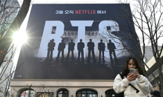 Une femme consulte son smartphone devant un panneau d'affichage annonçant le concert de retour du groupe de K-pop BTS, le 17 mars 2026 à Séoul ( AFP / Jung Yeon-je )