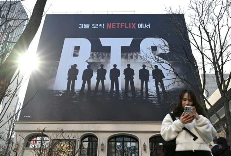 Une femme consulte son smartphone devant un panneau d'affichage annonçant le concert de retour du groupe de K-pop BTS, le 17 mars 2026 à Séoul ( AFP / Jung Yeon-je )