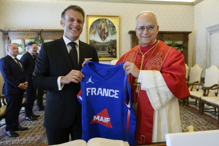 Photo prise et diffusée le 10 avril 2026 par Vatican Media montrant le président français Emmanuel Macron (g) offrant au pape Léon XIV, passionné de sport, un maillot dédicacé de l'équipe de France de basket-ball lors d'une audience privée au Vatican ( VATICAN MEDIA / Simone Risoluti )