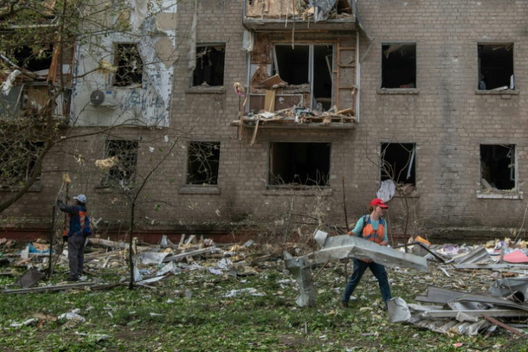 Des employés communaux ramassent des débris devant un immeuble résidentiel endommagé lors d'un bombardement russe à Dnipro, en Ukraine, le 18 mai 2026 ( AFP / Mykola SYNELNYKOV )
