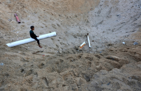 Un enfant palestinien est assis sur un bout d'une conduite d'eau dans un immense cratère provoqué par un raid israélien à Gaza-ville, le 28 juin 2025 ( AFP / Omar AL-QATTAA )