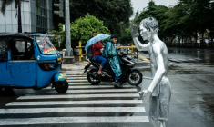 L'artiste de rue Ari Munandar (d), le corps recouvert de peinture argentée, fait la manche sous la pluie à un carrefour de Jakarta, le 1er avril 2025 en Indonésie ( AFP / Yasuyoshi CHIBA )