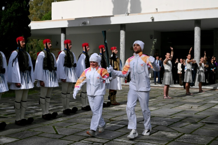 L'Italienne Stefania Belmondo et le Grec Petros Gaidatzis portent ensemble la flamme olympique à la sortie du musée du site antique d'Olympie, en Grèce, le 26 novembre 2025 ( AFP / Aggelos NAKKAS )