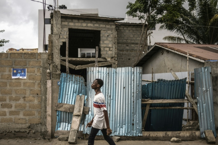 Un jeune homme marche dans un quartier de Cotonou le 9 avril 2026, près d'une affiche électorale placardée au mur  ( AFP / OLYMPIA DE MAISMONT )