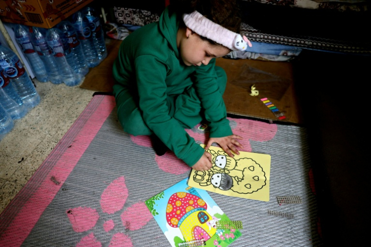 Une fillette colorie un dessin assise par terre dans une salle de classe d'une école publique transformée en refuge pour personnes déplacées, à Dekwaneh, au nord de Beyrouth, le 24 mars 2026 au Liban ( AFP / Anwar AMRO )