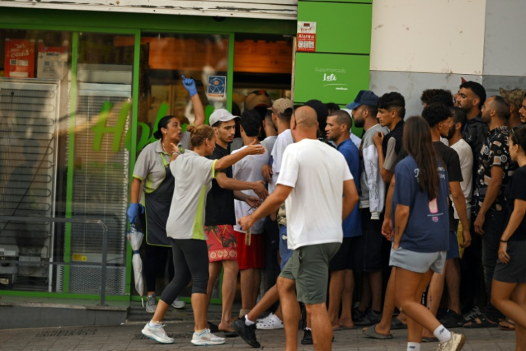 Des employés d'un supermarché (G) tentent de refouler des migrants cherchant à entrer dans le magasin dans l'enclave espagnole de Ceuta, le 1er août 2026 à Ceuta  ( AFP / JORGE GUERRERO )