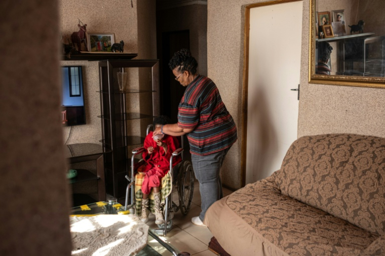 Lilly Stebe donne de l'eau à sa fille adoptive, Okuhle, née avec une paralysie cérébrale, dans leur maison de Snake Park, à Soweto, le 23 mai 2025 en Afrique du Sud ( AFP / EMMANUEL CROSET )