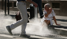 Une touriste assise à côté de la vapeur d'eau sortant d'une bouche d'aération dans le quartier de Wall Street, à New York, alors qu'une alerte à la chaleur extrême a été émise, le 23 juin 2025 ( AFP / TIMOTHY A. CLARY )