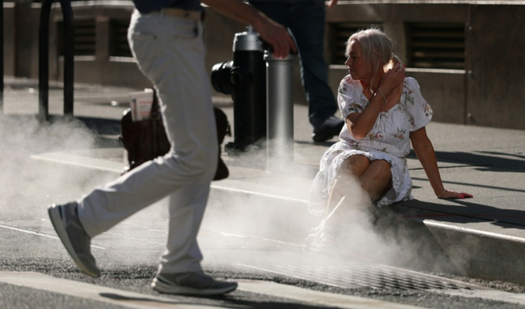 Une touriste assise à côté de la vapeur d'eau sortant d'une bouche d'aération dans le quartier de Wall Street, à New York, alors qu'une alerte à la chaleur extrême a été émise, le 23 juin 2025 ( AFP / TIMOTHY A. CLARY )