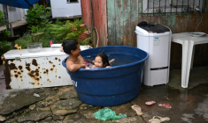 Une femme et sa fille se rafraîchissent dans une grande bassine remplie d'eau à Vila da Barca, un quartier pauvre bâti sur pilotis sur les rives du fleuve Guama à Belem, dans l'État du Para, le 5 novembre 2025 au Brésil ( AFP / Mauro PIMENTEL )