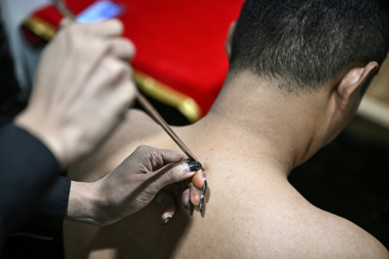 L'astrologue birman en exil Linn Nhyo Taryar marque d'un tatouage le dos d'un client, le 7 décembre 2025 à Bangkok  ( AFP / Lillian SUWANRUMPHA )