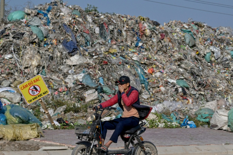 Un homme passe en deux-roues devant une montagne de déchets, en périphérie de Hanoï, le 25 novembre 2025 ( AFP / Nhac NGUYEN )