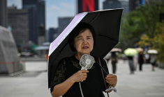 Une femme sous un parapluie avec un ventilateur portatif, le 12 juillet 2026 à Séoul  ( AFP / JADE GAO )