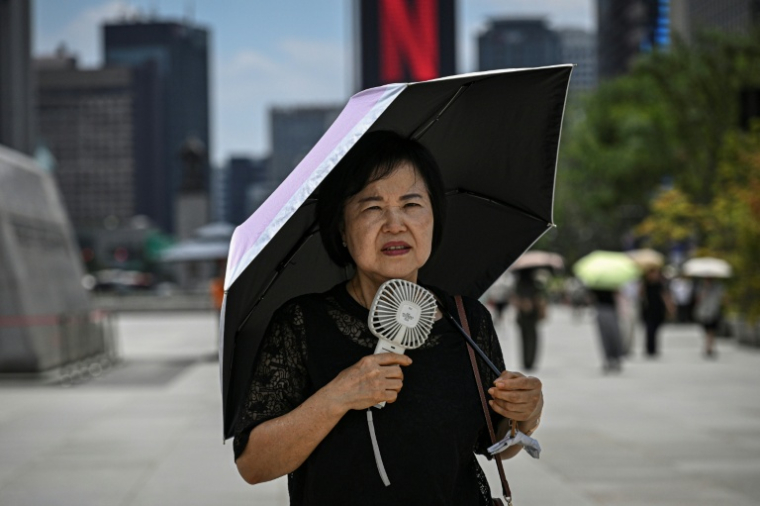 Une femme sous un parapluie avec un ventilateur portatif, le 12 juillet 2026 à Séoul  ( AFP / JADE GAO )