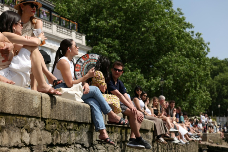 Des personnes assises au bord de la Tamise à Richmond, dans l'ouest de Londres, alors que les températures devraient grimper encore, le 23 mai 2026 au Royaume-Uni ( AFP / Adrian DENNIS )