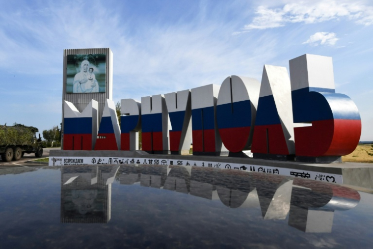 Un camion militaire russe passe devant les lettres géantes formant le mot Marioupol, peintes aux couleurs de la Russie, le 17 juillet 2025 dans la ville ukrainienne de Marioupol contrôlée par la Russie ( AFP / Olga MALTSEVA )