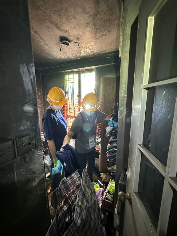 Sur cette photo prise et transmise le 23 avril 2026 par un habitant de Wang Fuk Court, Bowie Chan, son épouse Annie Tse (droite) passe en revue leurs affaires dans leur appartement endommagé par l'incendie de novembre, à Hong Kong ( Courtesy of Bowie Chan / Bowie Chan )