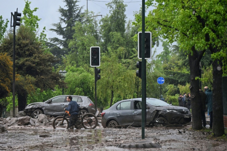 Un cycliste passe à côté de véhicules endommagés et partiellement ensevelis sous la boue et les débris après une coulée de boue dans le quartier de Las Condes, à Santiago, le 8 octobre 2026 ( AFP / RODRIGO ARANGUA )