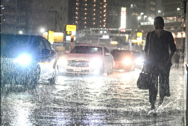 Des voitures dépassent un piéton sur une route inondée près de la station de métro de Chiba, dans la ville de Chiba à l'est de Tokyo, le 13 août 2026, alors que de fortes pluies s'abattaient sur la région ( AFP / Philip FONG )
