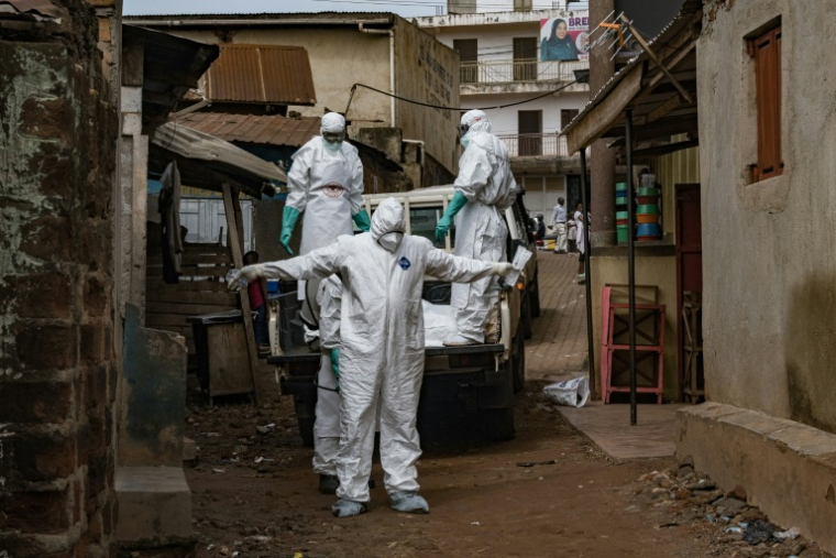 Des agents de la Croix-Rouge s'aspergent de désinfectant lors de l'évacuation du corps d'une victime présumée d'Ebola à Kampala, le 26 mai 2026 en Ouganda ( AFP / Badru KATUMBA )