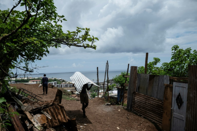 Un homme transporte une feuille de tôle dans le bidonville de Cavani, à Mamoudzou, à Mayotte, le 2 janvier 2025 ( AFP / JULIEN DE ROSA )