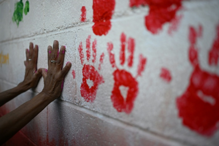La mère d'une personne disparue pose ses mains couvertes de peinture lors de l'inauguration d'une fresque en hommage aux personnes disparues, à l'Université du Salvador, à San Salvador, le 19 mars 2026 ( AFP / STRINGER )