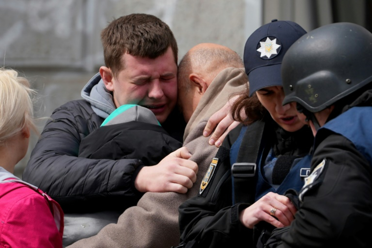 Deux hommes se réconfortent alors que des psychologues de la police ukrainienne offrent de l'aide aux habitants après une attaque russe de missiles à Soumy, dans le nord-est de l'Ukraine, le 13 avril 2025 ( AFP / Oleg VORONENKO )
